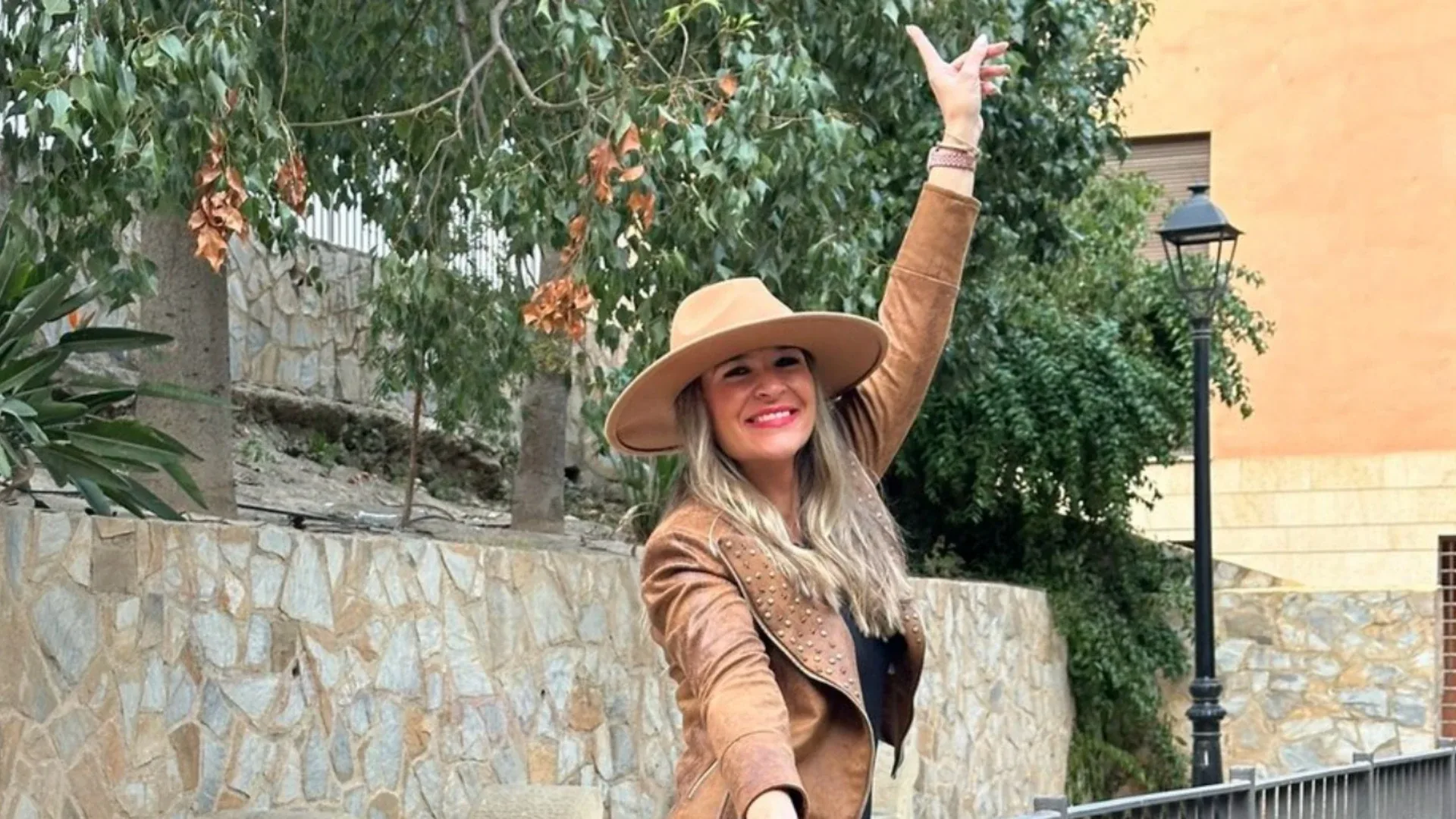 Isabel con sombrero y chaqueta ante un olivo